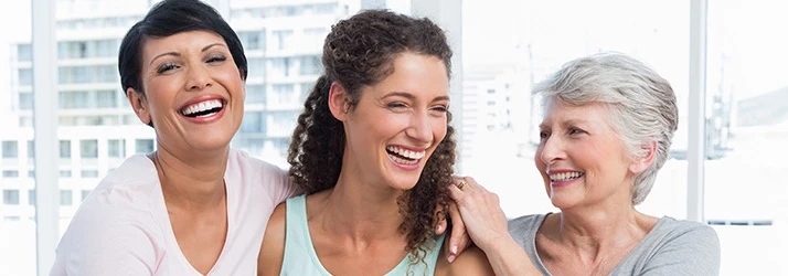 Three people sit together in a bright room, offering supportive connection across different generations.